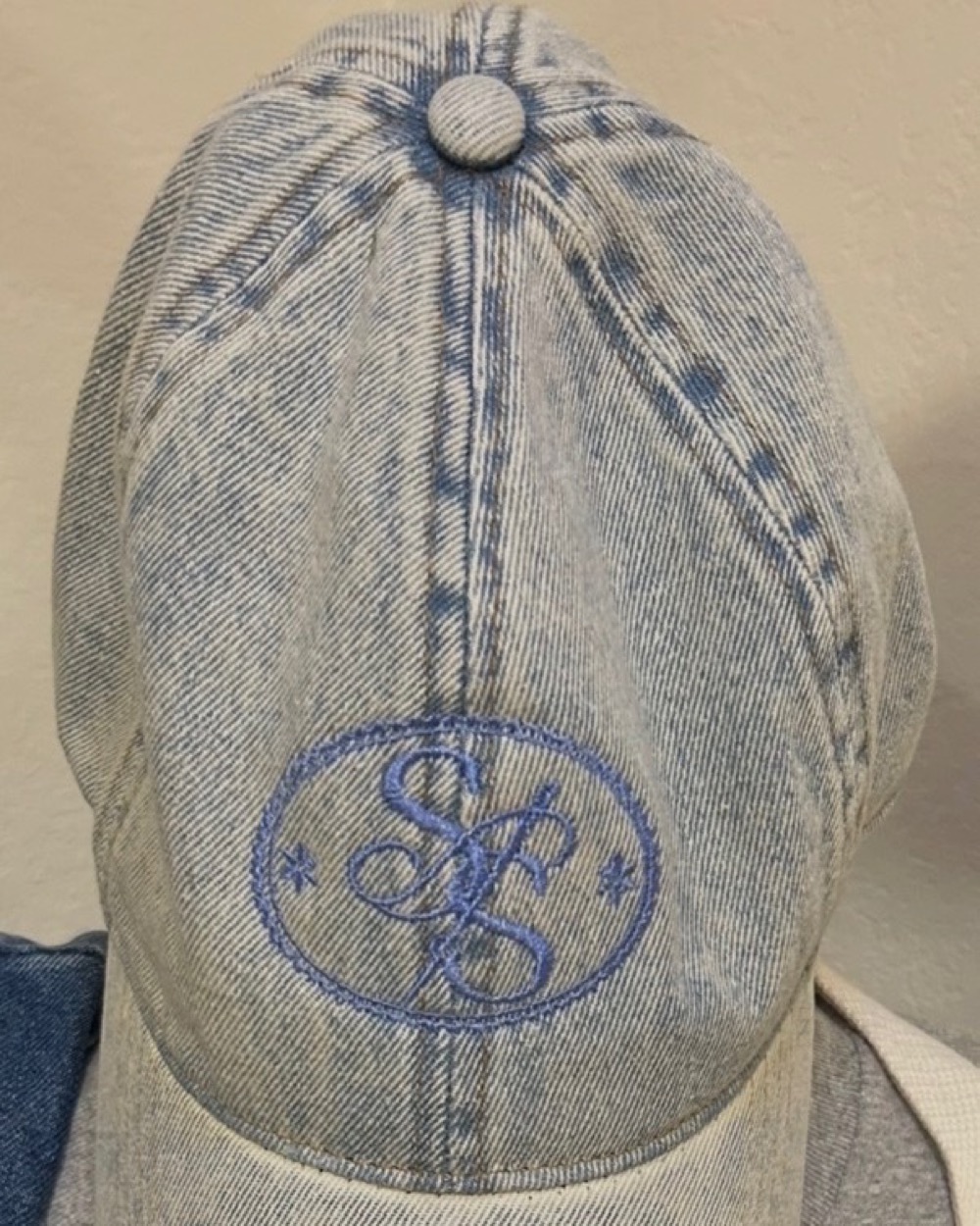 A light-wash denim cap embroidered with the Sister Stitch Society monogram in blue thread