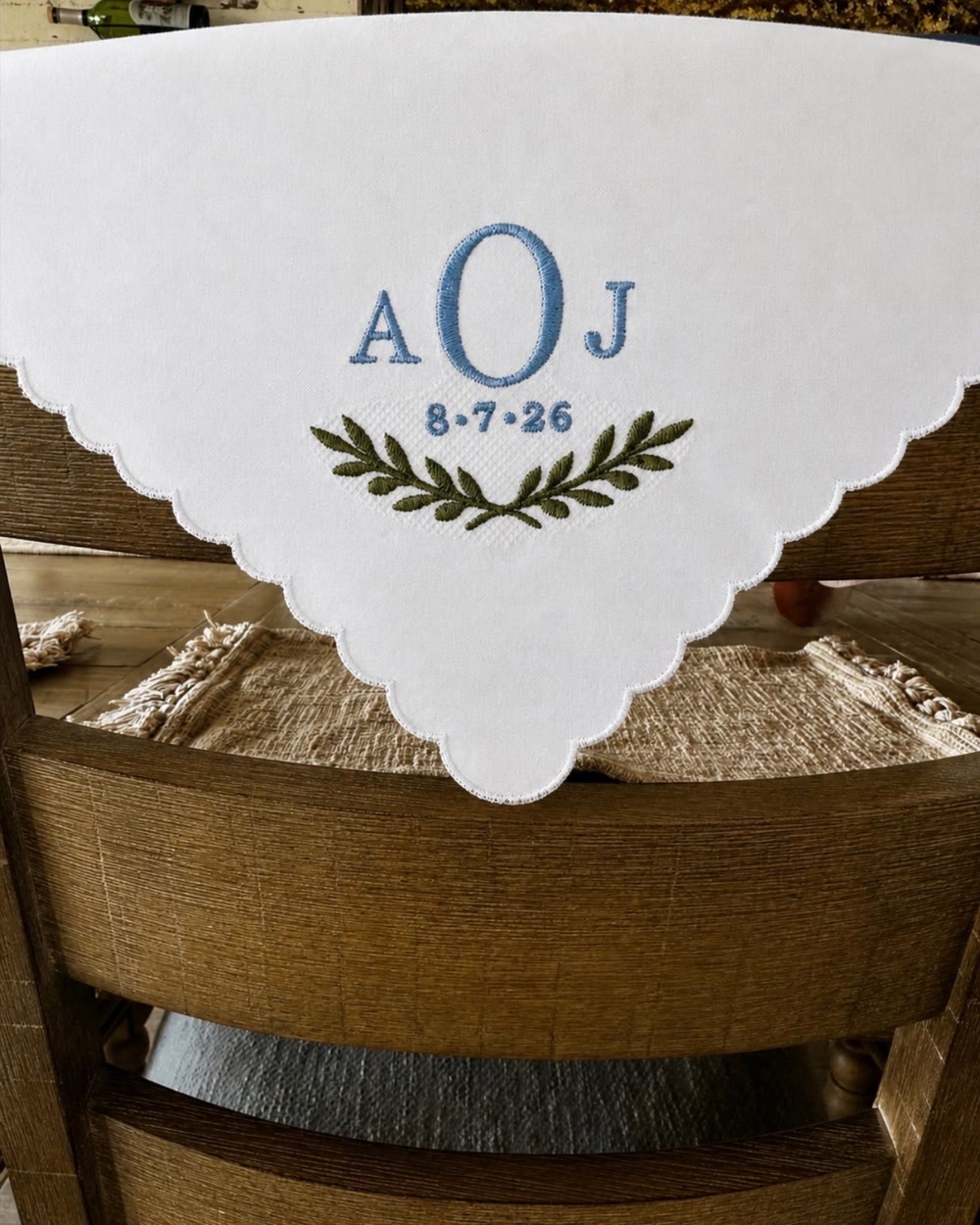 A white scalloped handkerchief embroidered with the monogram AOJ, a wedding date and a green laurel wreath