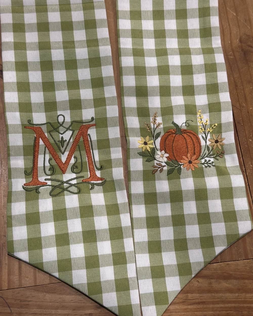 Sage gingham table runners embroidered with an ornate letter M and a pumpkin motif