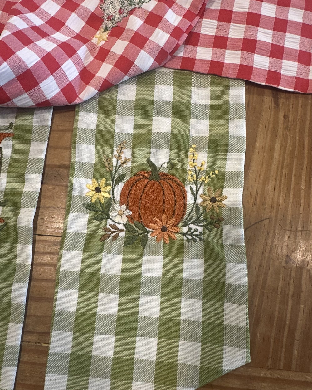 A sage gingham table runner embroidered with a pumpkin and autumn flowers