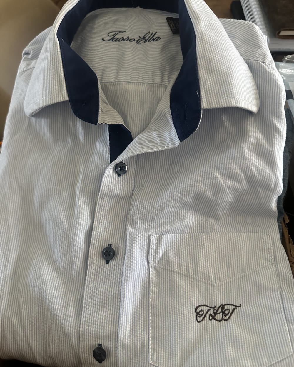 A white pinstriped shirt with a navy inner collar, embroidered with a script monogram above the chest pocket