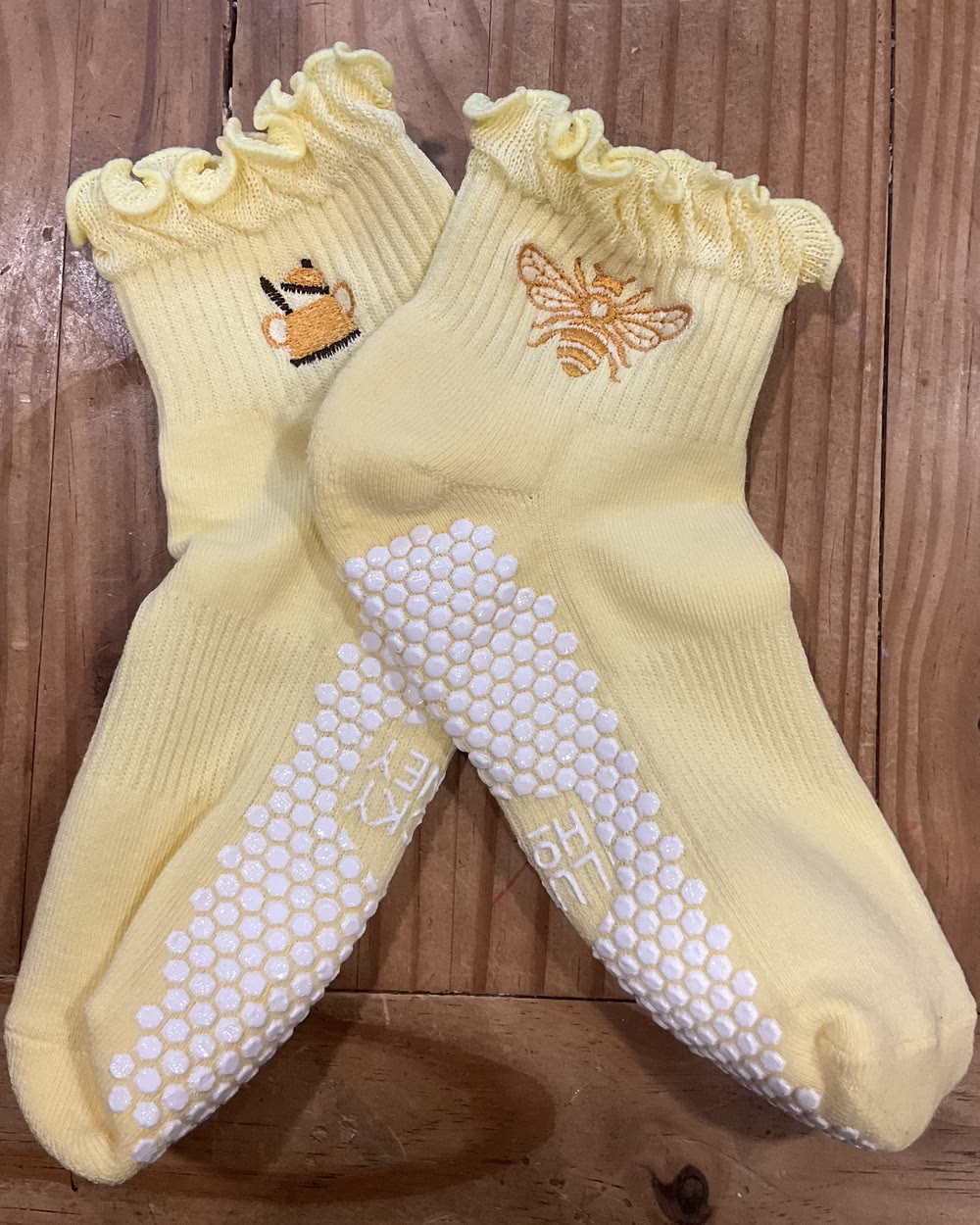 A pair of pale yellow ruffle grip socks, one embroidered with a honey pot and one with a bee