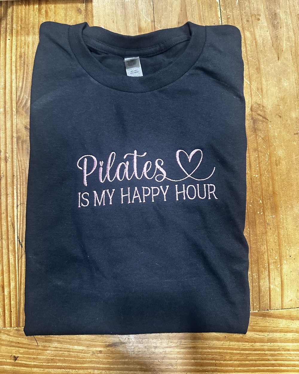 A navy sweatshirt embroidered in pink script reading Pilates is my happy hour