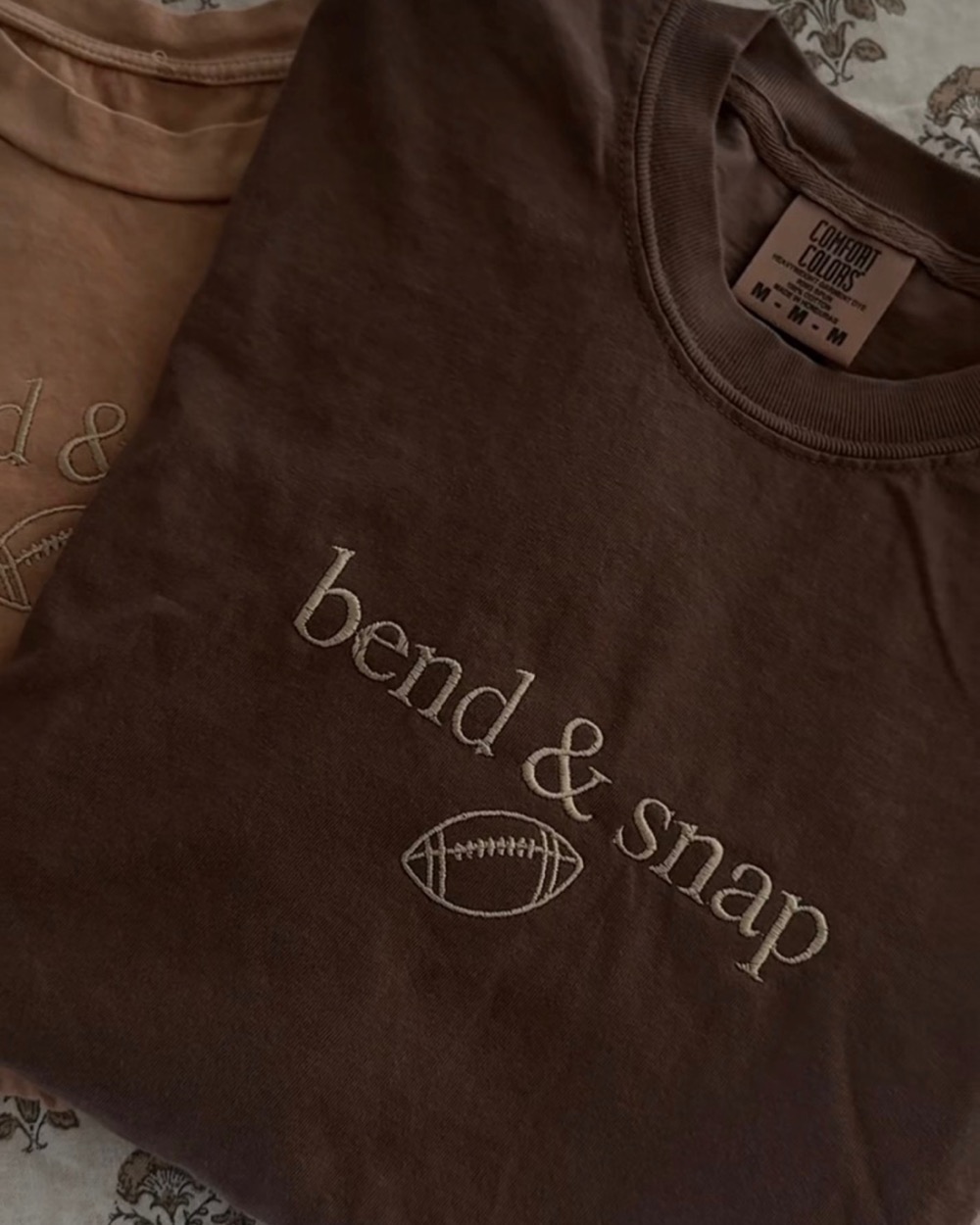 A brown tee embroidered bend and snap in cream, with a small football