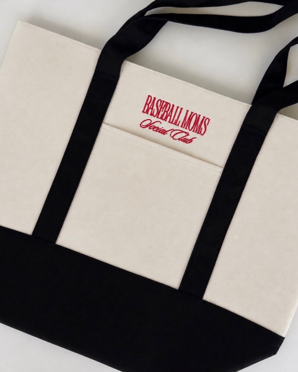 A cream and black canvas tote embroidered Baseball Moms Social Club in red