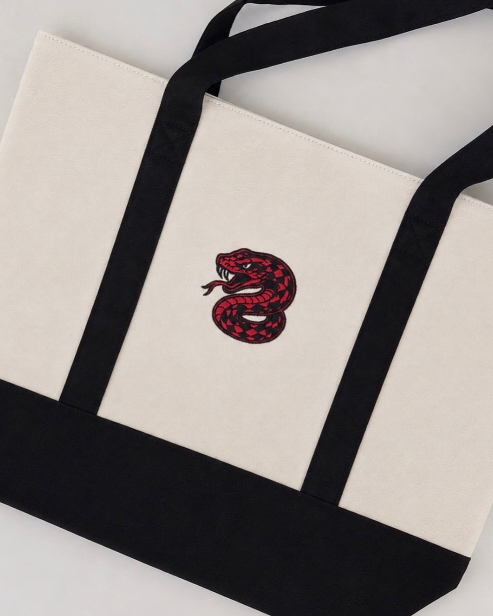 A cream and black canvas tote embroidered with a red and black snake